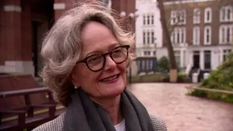 Elizabeth Campbell, the Conservative leader of Kensington and Chelsea council, wears glasses, suit jacket and a scarf and is standing in an area outside the council building