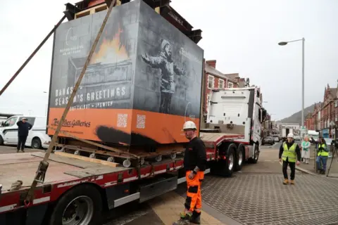Getty Images The covered artwork is secured on the back of a flatbed lorry with workmen in high vis jackets in a Port Talbot street.