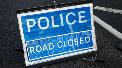 A blue sign which reads police road closed.
