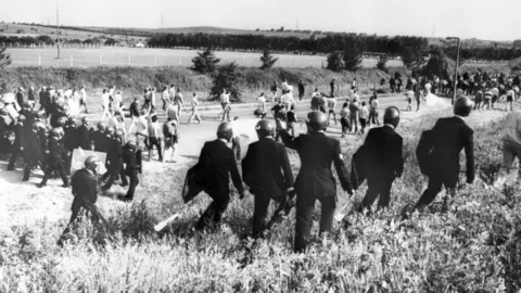 PA Media A black and white photo shows a line of police officers with shields confronting miners in normal clothes in a field.