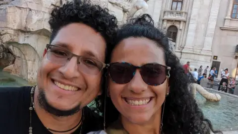 Adolfo and his wife in Venice - he has glasses on and a goate beard. She is smiling and wearing sunglasses.