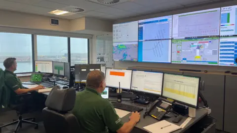 Ben Schofield/BBC Two operators sit in front of a bank of screens, displaying data about the East Anglia One wind farm