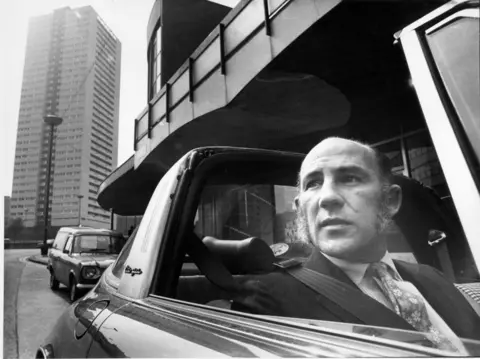 Getty Images Sir Stirling Moss pictured driving on the Smallbrook Queensway carriageways in 1972. He is in an open-topped car and is wearing his seatbelt, 