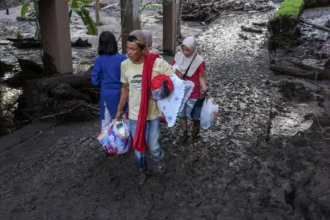 EPA Villagers carry their belongings as they walk through mud following a flash flood in Tanah Datar