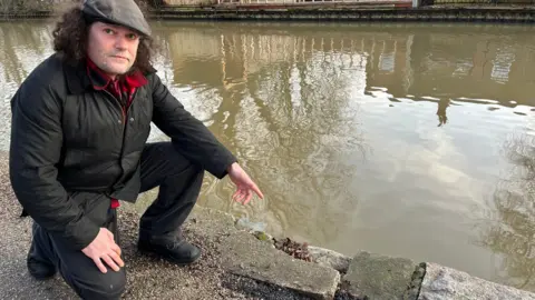 Chris Cooper pointing at the towpath damaged on Schwabisch Hall Way at Grand Union Canal, outside Boat Inn and near the Meadow Lane Bridge, in Leicestershire.