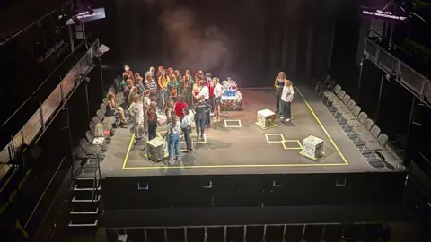 Brassneck Youth Theatre An aerial shot of the stage. The group is standing to the left and the stage is marked out with yellow tape. 