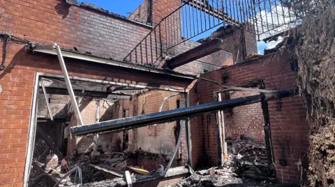 A fire damaged building with windows missing, collapsed beams and blackened walls