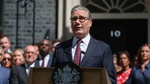 Reuters Keir Starmer wears a suit, glasses and has short grey hair. He stands at a lectern outside 10 Downing Street with a crowd of people behind him