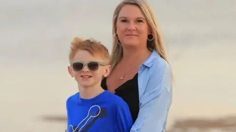 Supplied A woman with light hair on a beach hugging a child with ginger hair who has sunglasses on. 