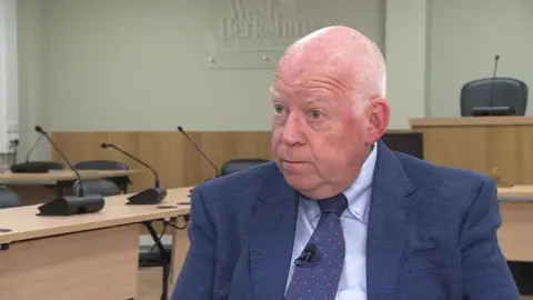 BBC Jeff Brooks - a man in a navy suit with a blue tie standing outside a building 