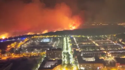 Aerial of red flames burning in mountain next to houses