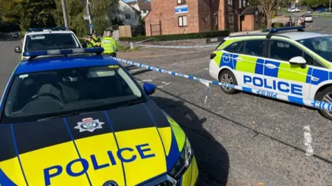 Several police officers and emergency vehicles are at a cordon around the scene of a murder investigation in Leicester