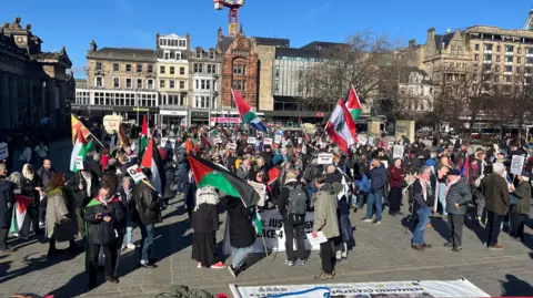A group of people standing in Edinburgh city centre waving Palestinian flags