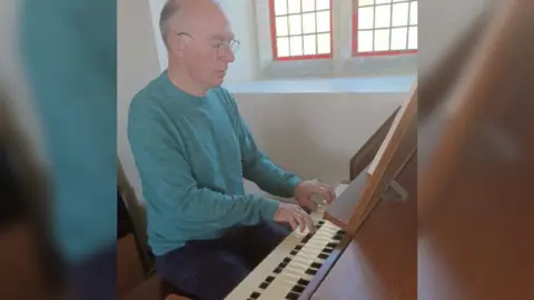 Mr Tomlinson in a blue jumper playing an electric organ