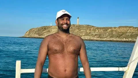 Prem's support crew Premal Pattani formerly from Swindon, standing on a boat after completing his swim of the Channel, with the sea and the Gap Gris-Nez in the background. 