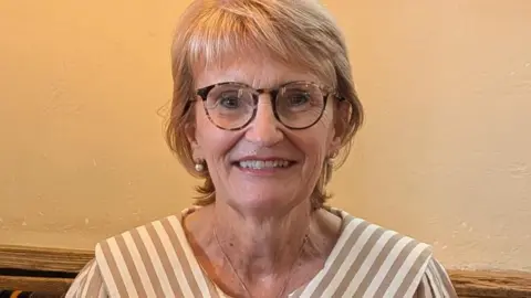 Denise Smith A woman who is wearing glasses is smiling at the camera.
