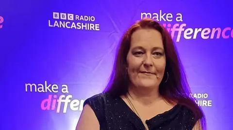 Beckie Ramsay A woman with dark hair and a glittery dress stands in front of a Make a Difference awards purple background with BBC Radio Lancashire written on it 