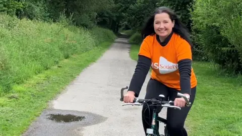 BBC Woman on a bike on the Camel Trail at Wenford Bridge wearing a bright orange multiple sclerosis t-shirt