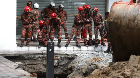 EPA Malaysia Fire and Rescue Department officers inspect the site where a woman fell into an 8m deep sinkhole in Kuala Lumpur