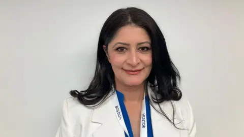 Shariqua Ahmed/BBC Head and shoulders image of Shabina Qayyum. She has long black hair and is wearing a white suit jacket.