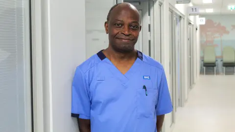 UWE A man smiles in a hospital ward, wearing a blue NHS nurse uniform.