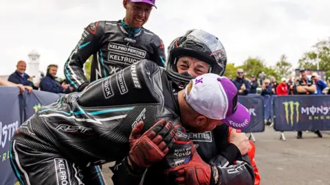 Isle of Man TT Races A sidecar crew in black leathers congratulating a man sitting in a red sidecar outfit