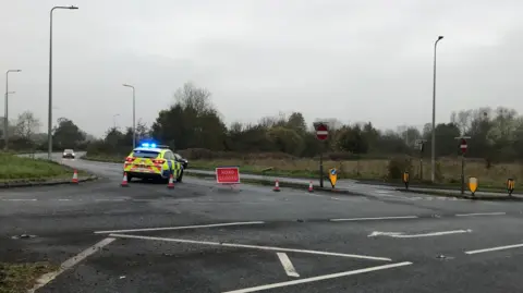 A police car, orange cones and a 'road closed' sign is blocking a main road.