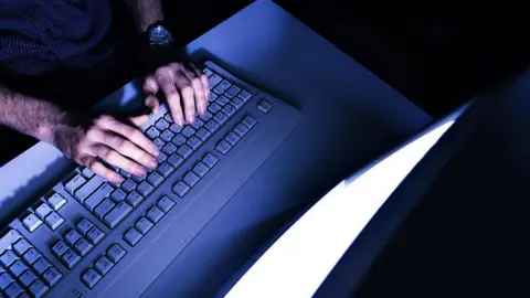 Getty Images A man places his hand on a computer keyboard while looking at a screen, his face is not in shot