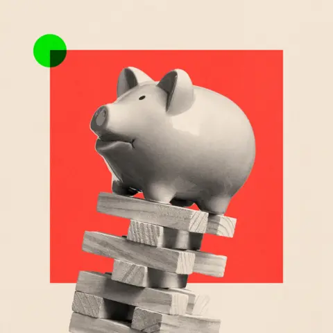 BBC A piggy bank balanced on top of some falling wooden blocks