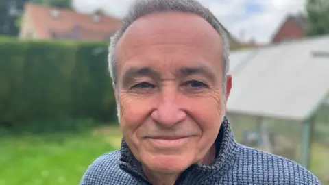BBC Stuart Downes smiling stood in the garden at his home in Lincolnshire reflecting on more than a year of being cancer free following successful immunotherapy. 