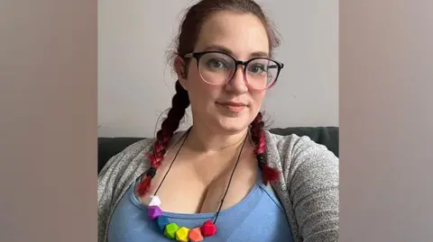 Kirstie looking at the camera, with two plaits, wearing a colourful necklace