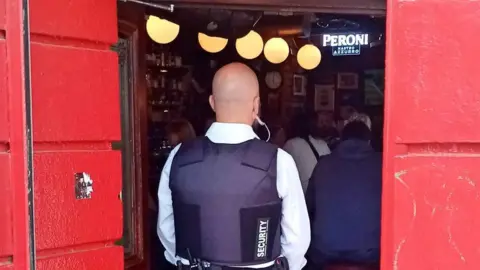 A member of security stands in a pub doorway with his back to the camera