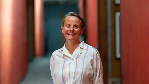 Lisa Whiting Paula Orrell, standing in a room with red columns and smiling for the camera.