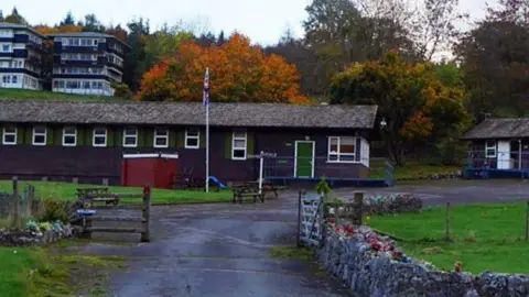 Exterior shot showing huts with a flag pole behind a dry stone walled entrance