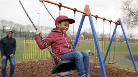 Getty Images Boy smiling on the swing and his father behind smiling
