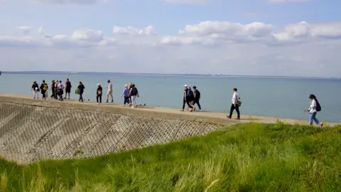 Serena Abbondanza A group of people walking along a wall with a body of water in the background.