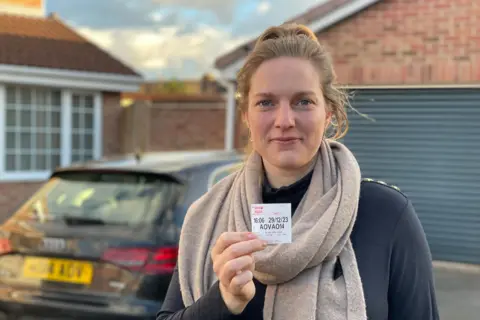 Sietske Sikkema holds up her parking ticket while standing next to her car