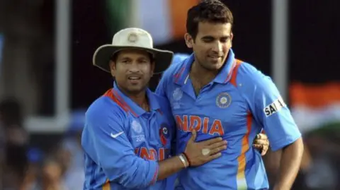 Getty Images Pemain kriket India Sachin Tendulkar (kiri) mengenakan seragam biru resmi tim India dan gelang baja serta topi mengucapkan selamat kepada rekan setimnya Zaheer Khan yang mengenakan seragam tim kriket India setelah merebut gawang batsman Australia Cameron White yang tak terlihat selama pertandingan perempat final Piala Dunia Kriket ICC 2011 antara India dan Australia di Stadion Sardar Patel, Motera di Ahmedabad pada 24 Maret 2011.