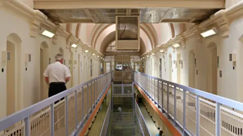 Corbis via Getty Images Rear of prison officer walking along a prison landing