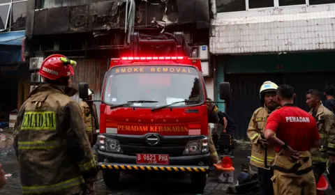 Firefighters stand next to a fire engine outside a badly burnt office block in Jakarta, Indonesia 