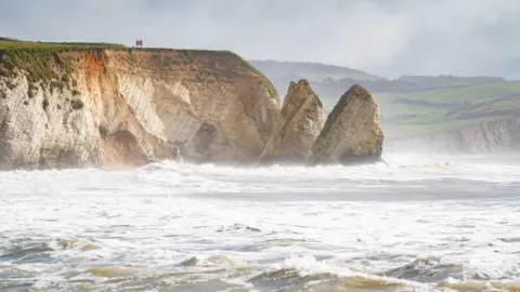 A view of the cave entrance at Freshwater Bay blocked after the cliff collapse. The sea appears choppy and the day is overcast.