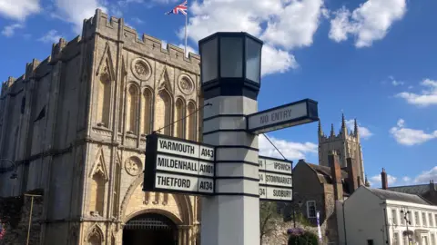 The gates to the Abbey gardens in Bury St Edmunds with a sign post in the foreground on Angel Hill.