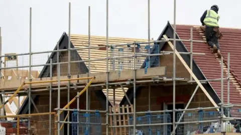 A man on a roof of a new home that is being built with scaffolding around it