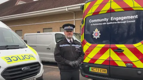 Inspector Matt Walton of Surrey Police stands in front of two police vans.