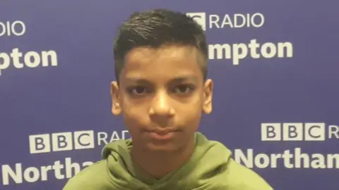 Kautilya Katariya standing in front of a BBC Northampton board, wearing a green hoodie 