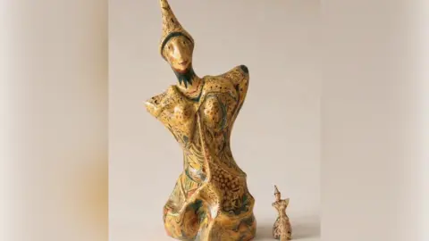 A large sculpture of a person with no arms and legs, wearing a hat and with a smile on their face. It has been decorated with a unique pattern. A miniature version has been placed next to it.