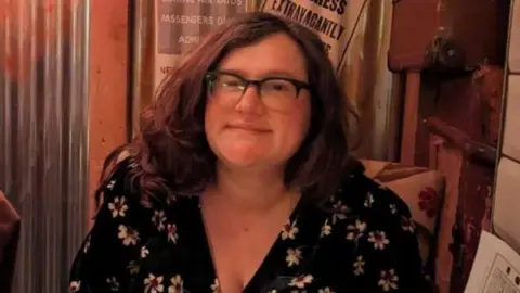 Alice Topping Head and shoulders image of Alice Topping wearing a black top with white flowers
