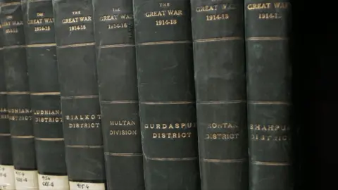 Seven leather bound books in a line, with the names of different districts on them, all with the title 'The Great War 1914-1918' on them.