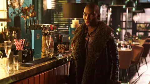 BBC/ Various Artists Ltd and FALKNA Michaela Coel's character Arabella wearing a fur and leather jacket at a bar