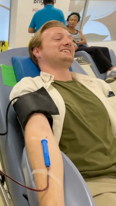 Young man in a green t-shirt lying down giving blood with tube connected to arm